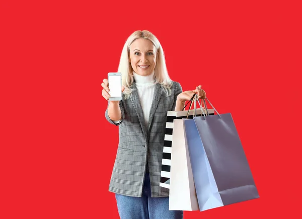Rijpere Vrouw Met Mobiele Telefoon Boodschappentassen Rode Achtergrond — Stockfoto