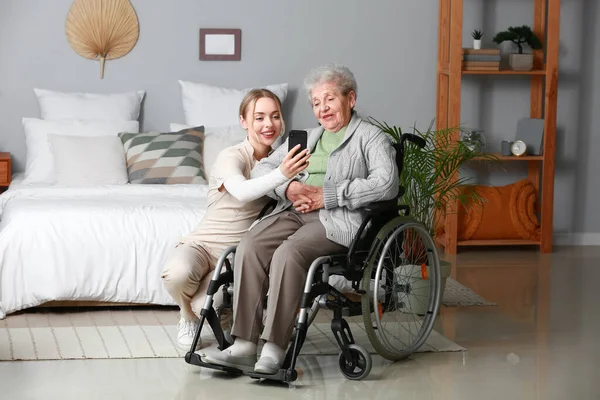 Tekerlekli Sandalyedeki Yaşlı Kadınla Evde Cep Telefonu Kullanan Genç Bir — Stok fotoğraf