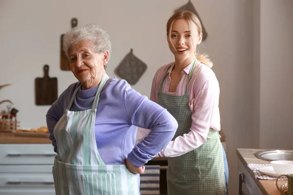 Young woman tying apron of her grandmother in kitchen