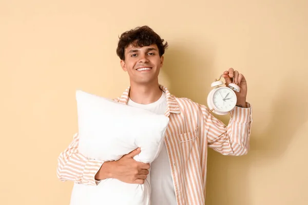 Young man with pillow and alarm clock on beige background