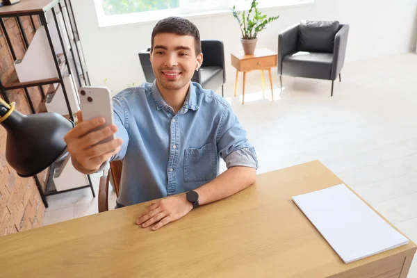 Young man with mobile phone video chatting in office