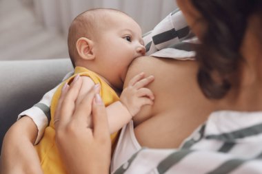 Genç bir kadın bebeğini evde emziriyor.