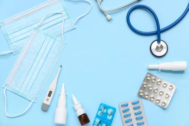 Mavi arka planda ilaç, termometre ve tıbbi maskeli burun damlası şişeleri.