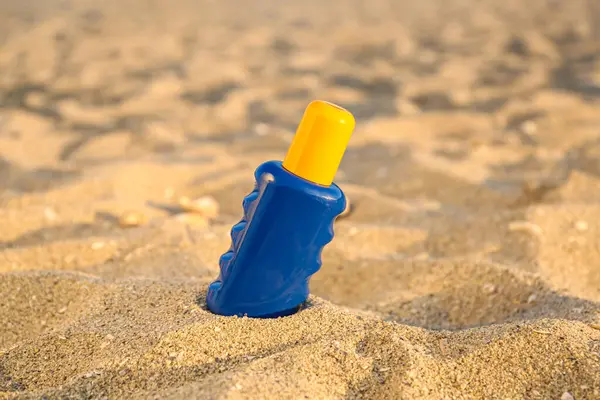 Bottle of sunscreen cream on sand at sea beach