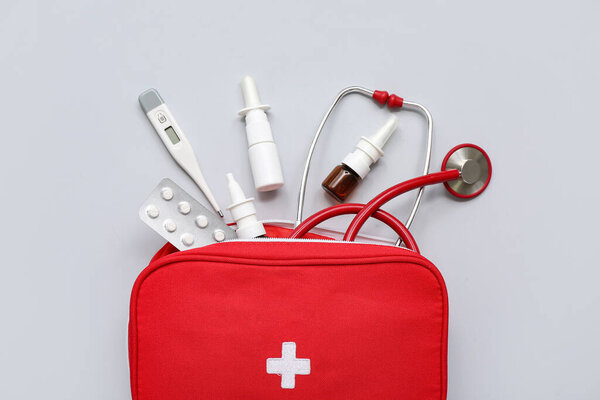 First aid kit with nasal drops, thermometer, pills and medical stethoscope on grey background