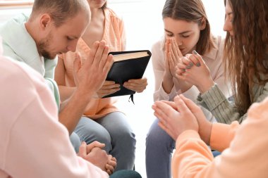 Group of people praying with Holy Bible in room