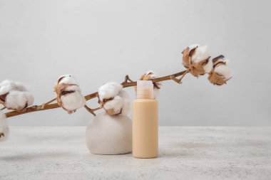 Hafif arkaplanda bir şişe kozmetik ürünü, sıva podyumu ve pamuk dalı