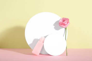 Kozmetik ürün şişesi, alçı podyumlar ve arkaplandaki gül çiçeğiyle kompozisyon