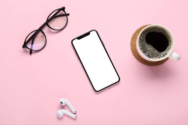 Modern cep telefonu, kulaklık, gözlük ve pembe arka planda bir fincan kahve.