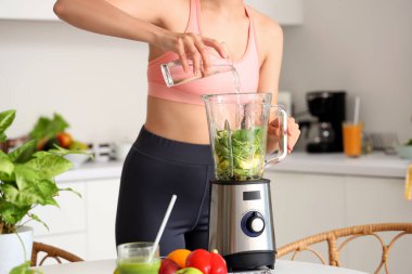 Sportif genç bayan mutfakta blender ile sağlıklı smoothie yapıyor, yakın plan.