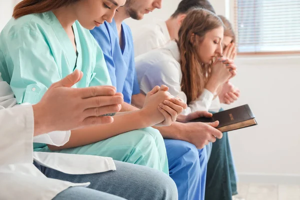 Group of doctors praying with Holy Bible in clinic, closeup