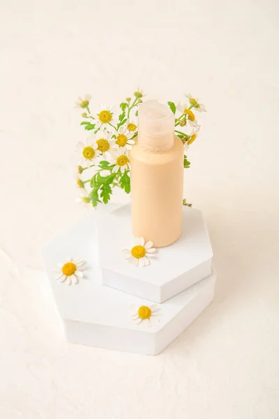 Composition with bottle of cosmetic product, plaster podiums and chamomile flowers on light background