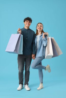 Mavi arka planda alışveriş torbaları olan mutlu genç bir çift.