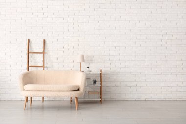 Tuğla duvarın yanında merdiveni olan rahat beyaz kanepe ve raf ünitesi.