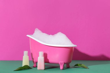 Sabun köpüklü küçük küvet ve renkli arka planda kozmetik ürünler.