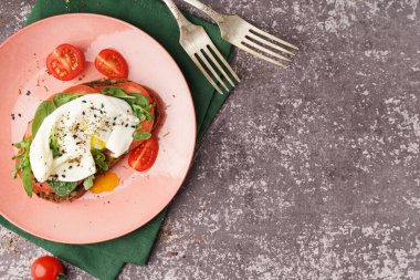 Gri zemin üzerinde yumurta olan lezzetli bir sandviç tabağı.