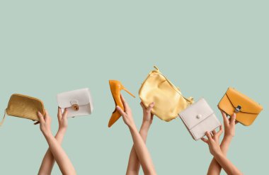 Birçok kadın eli farklı şık çantalar ve açık yeşil arka planda yüksek topuklu ayakkabılar taşıyor.