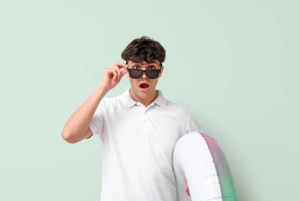 Zszokowany Młody Człowiek Okularach Przeciwsłonecznych Nadmuchiwanym Pierścieniu Zielonym Tle — Zdjęcie stockowe