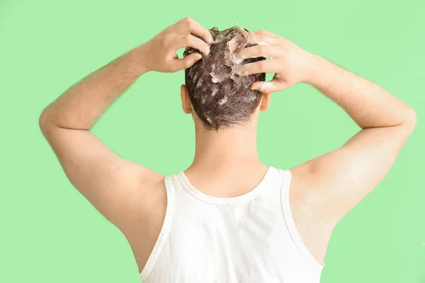 Young man washing hair against green background, back view