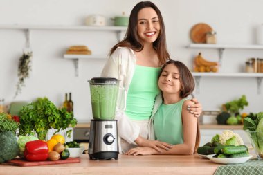 Küçük kız ve annesi mutfakta blender ile sebze suyu yapıyorlar.