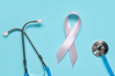 Renkli arka planda pembe farkındalık kurdelesi ve steteskop, yakın plan. Göğüs kanseri kavramı