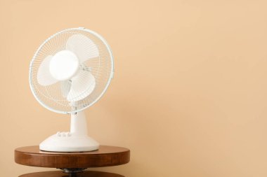 Bej duvarın yanında modern elektrikli fanı olan ahşap bir sehpa.