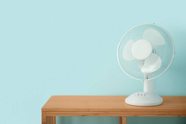 Mavi duvarın yanında modern elektrikli vantilatörü olan ahşap masa.