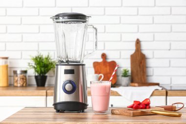 Modern blender ve bir bardak lezzetli çilekli smoothie mutfaktaki masada.