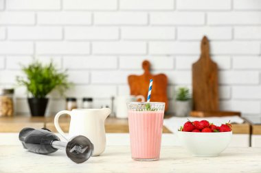 Modern blender ve bir bardak lezzetli çilekli smoothie mutfaktaki masada.