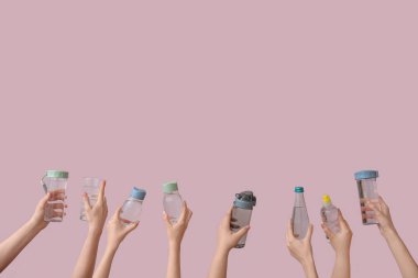 Şişeli kadın elleri ve pembe arka planda bir bardak soğuk su.