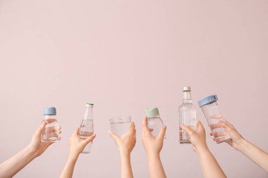 Şişeli kadın elleri ve pembe arka planda bir bardak soğuk su.