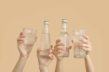 Şişeli kadın elleri ve bej arka planda bir bardak soğuk su.