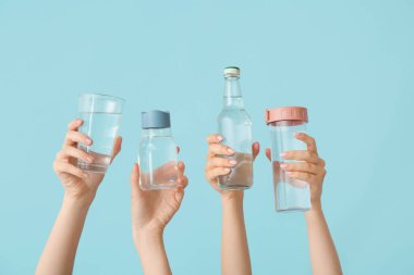 Mavi zemin üzerinde şişe ve bir bardak soğuk su olan kadın elleri.