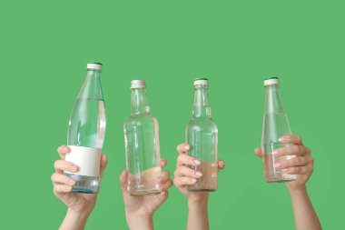 Yeşil arka planda soğuk su şişeleri olan kadın eller.