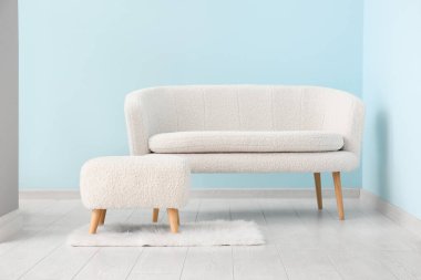 Mavi duvarın yanında beyaz kanepe ve puf.