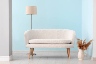 Beyaz kanepe, vazo, otlar ve mavi duvarın yanında standart lamba.