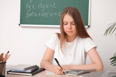 Genç matematik öğretmeni sınıftaki tahta masada öğrencinin ödevlerini kontrol ediyor.