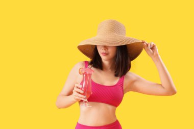 Mayo giymiş güzel Asyalı kadın ve sarı arka planda kokteyl.