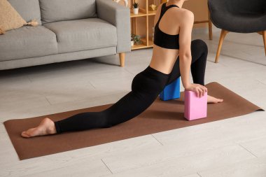 Evde bloklarla yoga yapan genç bir kadın.