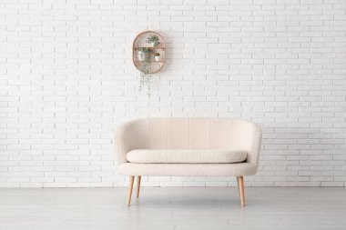 Rahat beyaz kanepe ve tuğla duvarın yanındaki bitkilerle dolu raflar.