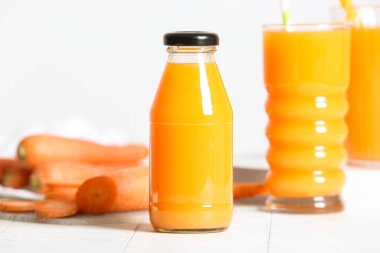 Beyaz fayans masasında şişe ve bir bardak taze havuç suyu.