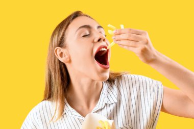 Beautiful young woman eating french fries on yellow background