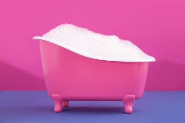 Renkli sabun köpüğüyle küçük pembe bir küvet.