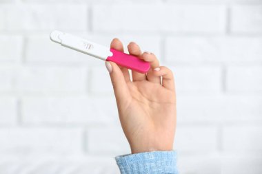 Hafif tuğla duvara karşı hamilelik testi pozitif olan kadın eli, yakın plan.