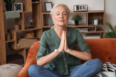 Olgun kadın evdeki kanepede meditasyon yapıyor.