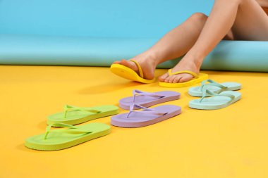 Renkli arka planda farklı renk parmak arası terlikleri olan kadın bacakları