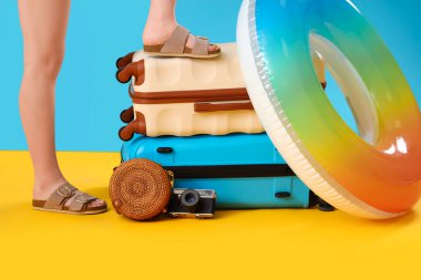 Farklı bavulları ve renkli arka planda plaj aksesuarları olan şık sandaletli kadın bacakları.