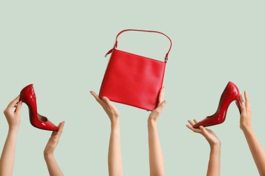 Şık bir çanta taşıyan ve açık yeşil arka planda yüksek topuklu giyen bir kadın.