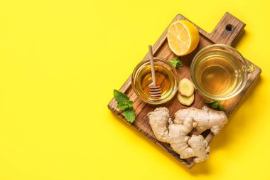 Sarı zemin üzerinde bal olan bir bardak zencefil çayı ve kase.