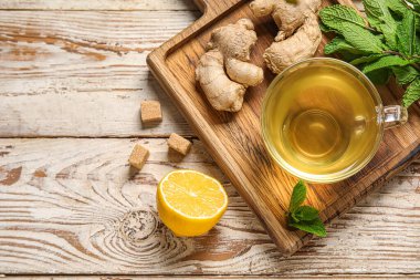 Beyaz ahşap zemin üzerinde limonlu ve naneli bir bardak zencefil çayı.